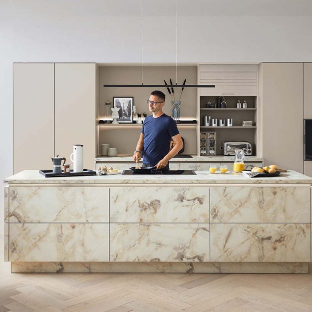 Hochwertige Designküche mit großzügiger Kochinsel in edler Marmoroptik, kombiniert mit hellen Fronten und offenen Nischen – modern, elegant und wohnlich zugleich