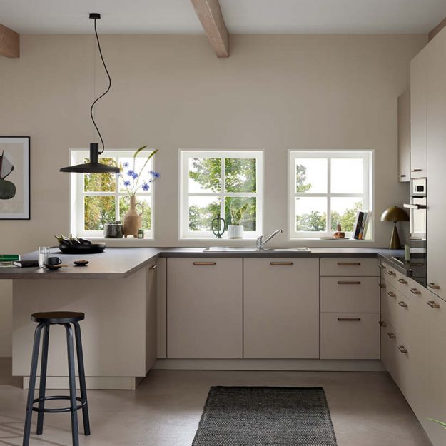 Zeitlose Küche in warmen Beigetönen mit klarer Linienführung, funktionaler L-Form und integriertem Sitzbereich – harmonisch ergänzt durch natürliche Materialien und viel Tageslicht