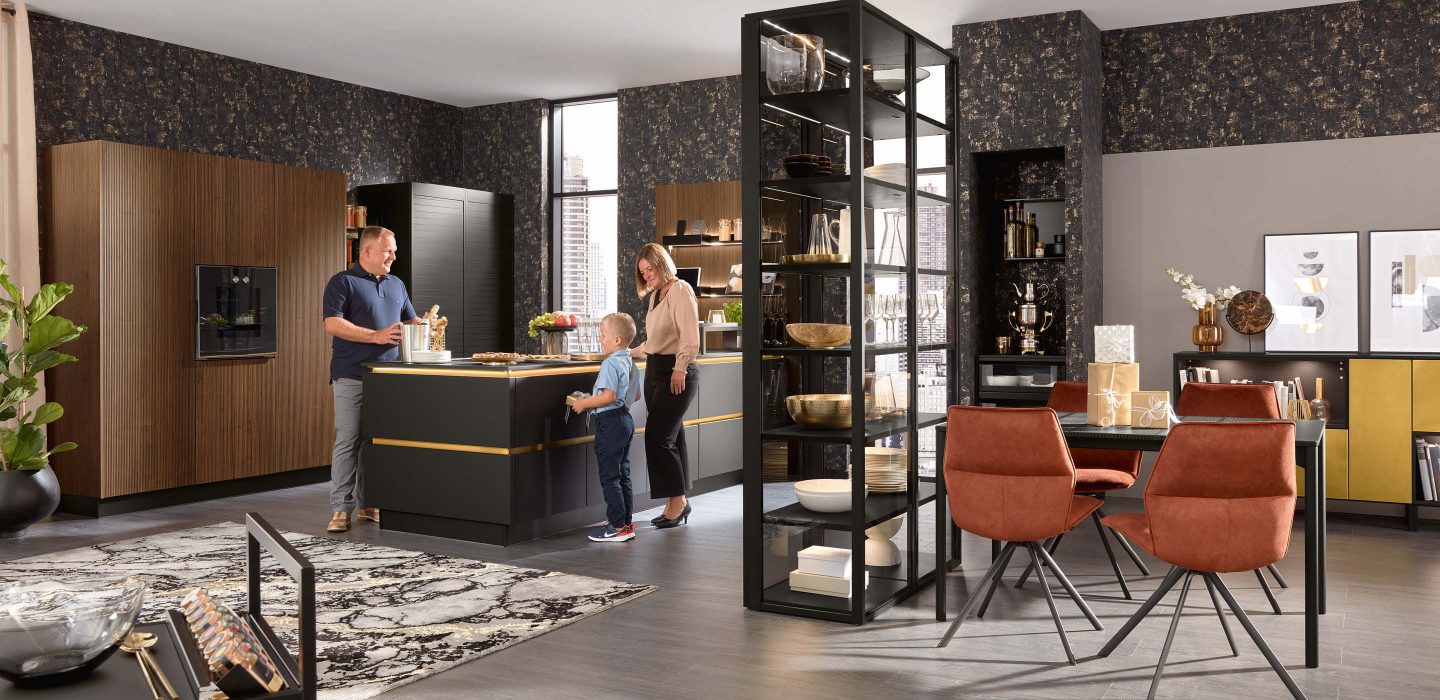 Moderne Designküche mit dunklen Fronten, Familie beim gemeinsamen Kochen und großzügigem Essbereich mit Glasvitrine und stilvollen Möbeln