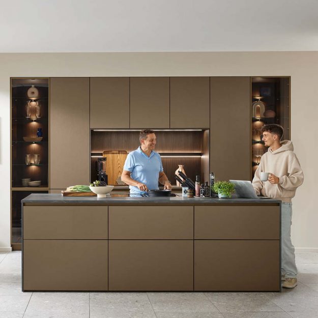 Moderne Ballerina Küche in warmen Braun- und Naturtönen mit großzügiger Kochinsel und integrierter Beleuchtung – ideal für gemeinsames Kochen und Wohnen