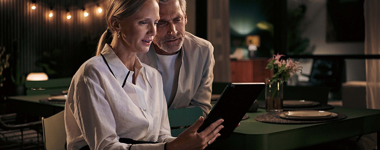 Paar betrachtet Tablet im Küchenstudio Bodensee Küchen Markdorf bei Einbauküche mit Geräten von Siemens und gedecktem Tisch im Hintergrund