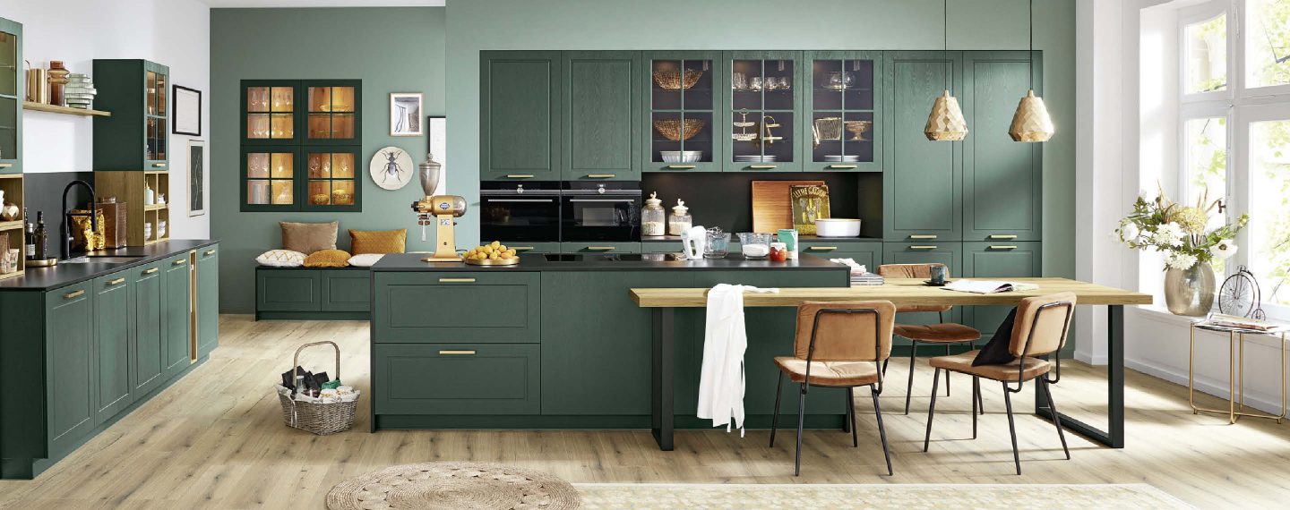 Moderne Landhausküche in elegantem Grün mit klassischen Kassettenfronten, integrierter Kochinsel und Essplatz, kombiniert mit warmen Holz- und goldenen Akzenten für eine stilvolle, wohnliche Atmosphäre