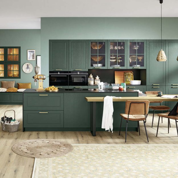 Stilvolle Landhausküche in dunklem Grün mit integrierter Kochinsel und Essbereich, kombiniert mit warmen Materialien und eleganten Details